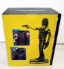 The image shows the side of a product box for a Cyberpunk 2077 figure. The box is yellow with black text and graphics. A figure of the character 'Silberhand' is depicted on the right side of the box, holding a gun. Two inset images on the left show details Náhled obrázku produktu