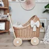 A wicker doll carriage with a bow decoration, placed in a nursery or play area. Anteprima dell’immagine prodotto