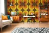 A retro-style living room with a patterned wallpaper, sofa, desk, and shelving unit. Produktbild-Vorschau