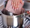 A hand is shown scrubbing the inside of a stainless steel pot with a copper-colored scrubber. Anteprima dell’immagine prodotto