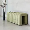 A green upholstered bench with a book on top, placed next to a tall black vase with dried branches in a minimalist interior. Produktbild-Vorschau