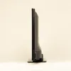 Side view of a black flat-screen television on a stand, set against a plain cream background. Produktbild-Vorschau