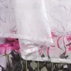 A close-up view of a white sheer curtain with a floral pattern, layered over a bouquet of pink roses. Produktbild-Vorschau