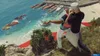 Two people are on a cliff overlooking a body of water with boats. Produktbild-Vorschau
