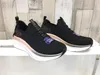 A pair of black Skechers sneakers with rose gold accents and white soles are displayed on a white shelf against a light wood-paneled background. Náhled obrázku produktu