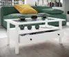A modern living room scene featuring a white coffee table with a glass top, a green sofa with a yellow cushion, and decorative items on the table. Produktbild-Vorschau