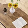 A close-up view of a wooden table with a glass of red wine, a white vase with sunflowers, and an open book. Produktbild-Vorschau