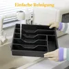 A person is rinsing a black cutlery organizer under a faucet in a kitchen sink. Produktbild-Vorschau