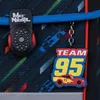 A close-up of a backpack strap with a "McNeill" brand tag and a "Team 95" keychain featuring a cartoon race car. Anteprima dell’immagine prodotto