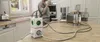 A person is in a kitchen, drinking from a mug, with various kitchen appliances and a power strip on the counter. Produktbild-Vorschau