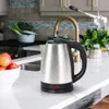 A stainless steel electric kettle sits on a kitchen countertop next to a bowl of fruit. Produktbild-Vorschau