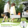A family is walking towards a car with the trunk open, carrying picnic items and a white folding bench. The scene is set in a grassy outdoor area with trees in the background. Produktbild-Vorschau