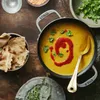 A top-down view of a pot of lentil soup with naan bread and cilantro on a wooden table. Produktbild-Vorschau