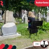 A person sits on a black metal bench in a cemetery, with gravestones and trees in the background. Produktbild-Vorschau