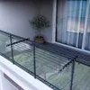 A clothes drying rack is attached to a balcony railing, with a potted plant and sliding glass doors in the background. Produktbild-Vorschau
