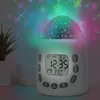 A white alarm clock with a star projector is shown on a table, projecting colorful stars onto the ceiling. A plant is visible in the background. Produktbild-Vorschau
