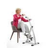 An older woman is exercising on a stationary bike while sitting on a chair. Produktbild-Vorschau