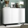 A white cabinet with three doors and black legs, decorated with various items on top, set against a green wall. Produktbild-Vorschau