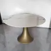 A round dining table with a marble-like ceramic top and a gold pedestal base is shown against a white wall and gray floor. Produktbild-Vorschau
