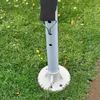 A close-up view of the base and lower pole of a pavilion or party tent, set up on a grassy area with some yellow flowers. Produktbild-Vorschau