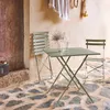A bistro set on a stone patio with a rustic wall and door. Produktbild-Vorschau