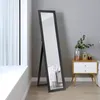 A full-length mirror with a black frame stands in a room next to a nightstand with decorative items.
