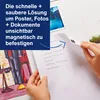 A person's hands are holding a piece of paper with a handwritten list, and a magnetic square is attached to the corner of the paper. The paper is being placed on a surface with other items like photos and a drawing. A blue text box with marketing informati Náhled obrázku produktu
