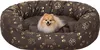 A small dog is resting in a brown oval dog bed with a gold paw print pattern. Podgląd zdjęcia produktu