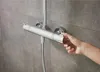 A hand is shown adjusting a chrome shower mixer with a grey tiled wall in the background. Produktbild-Vorschau