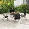 A patio set with four chairs and a table is arranged on a paved patio surrounded by lush greenery. Náhľad obrázku produktu