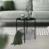A round black metal side table with a gray fabric basket and a green blanket draped over it, placed on a striped rug next to a light gray sofa.
