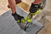 A person wearing work gloves is using a Ryobi angle grinder to cut a stone slab. Dust is flying from the cut. Produktbild-Vorschau