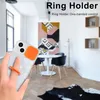 A hand holding a phone with a ring holder attached, in a modern living room setting. Produktbild-Vorschau