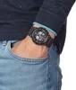 A person's wrist wearing a black G-Shock watch with red accents, with their hand in their jeans pocket. Náhľad obrázku produktu