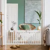 A white wooden pet gate is set up in a doorway, with a chair and plant in the background. Produktbild-Vorschau