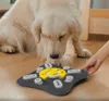 A golden retriever dog is looking down at a dog puzzle toy on the floor, with a person's hand reaching towards the toy. Produktbild-Vorschau