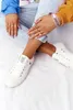 A person wearing white sneakers and jeans, sitting with their legs crossed. Podgląd zdjęcia produktu
