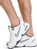 A close-up shot of a pair of white Nike Air Monarch IV sneakers on a person's feet. Náhled obrázku produktu