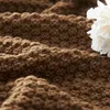A close-up view of a brown knitted blanket with a white flower on the right side. Anteprima dell’immagine prodotto