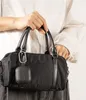A person is holding a black handbag with a black earbud case attached to it. Voir les images du produit