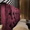 A close-up view of a tufted burgundy velvet headboard of a bed, with pillows and a wall in the background. Produktbild-Vorschau