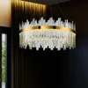 A luxurious chandelier with crystal elements and a gold band hangs in a dimly lit room with dark walls and a window with greenery visible. Produktbild-Vorschau