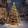 A decorated Christmas tree with lights and ornaments stands in the snow next to a wooden house. Náhled obrázku produktu