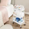 A white rolling cart filled with baby supplies next to a bed. Náhled obrázku produktu