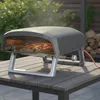 A pizza oven on a wooden table outdoors, with a pizza inside. Produktbild-Vorschau