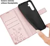 A hand is holding a black phone case over an open rose gold wallet case with card slots and a butterfly design. Produktbild-Vorschau