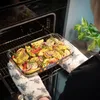 A person is placing a glass baking dish filled with potatoes, red peppers, and red onions into an oven. Podgląd zdjęcia produktu