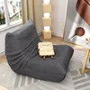 A cozy living room scene featuring a large gray beanbag chair with a toast-shaped pillow on it, next to a floor lamp and a piece of abstract art. Produktbild-Vorschau