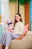 A young girl is holding a pink plush toy while sitting on a beanbag chair. Náhľad obrázku produktu