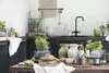 A kitchen counter with various items including pitchers, olive oil bottles, bread, and herbs. Produktbild-Vorschau